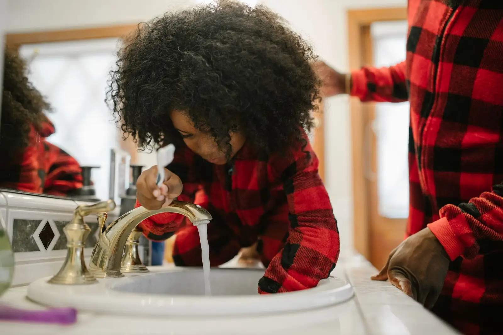 A father helping his daughter brush her teeth at the bathroom sink