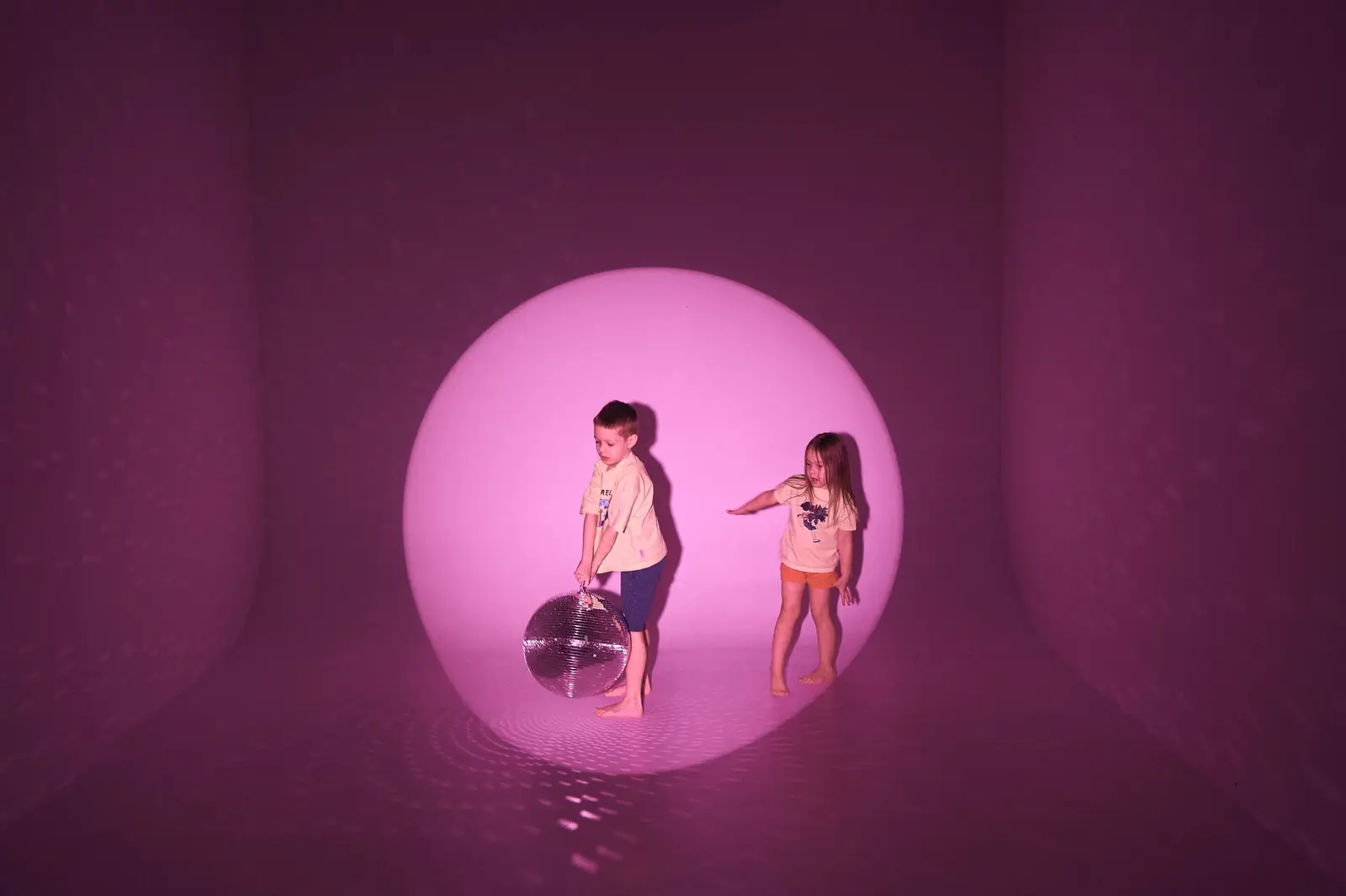 Two children playing in a softly lit pink room with a glowing light