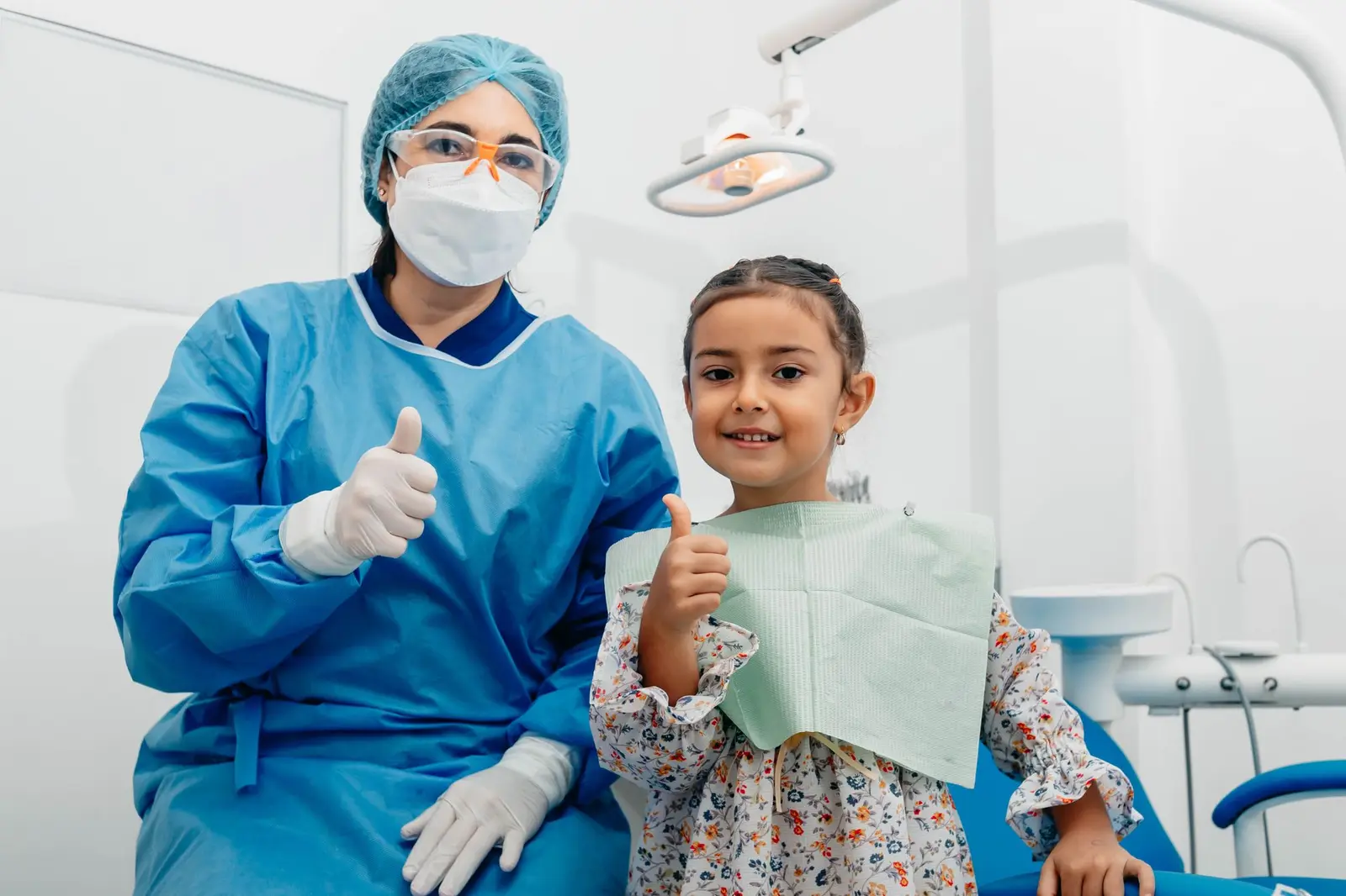 A dentist and a smiling girl giving thumbs up in a dental clinic