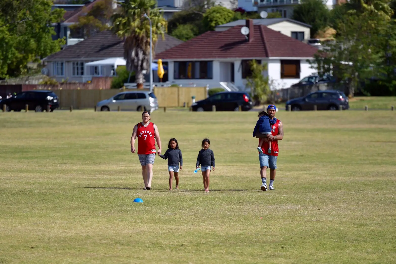 A family walking across a grassy park with houses behind