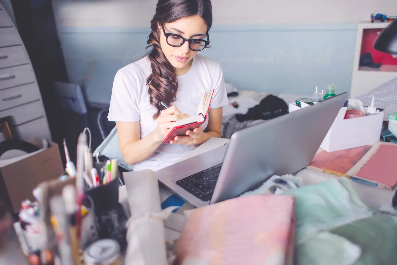 A young woman in glasses studying at a desk with a laptop and notebook