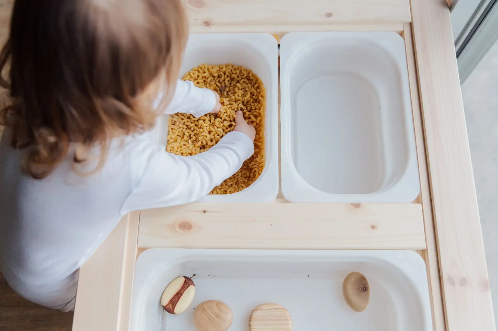A young child exploring a bin of dry pasta during sensory play