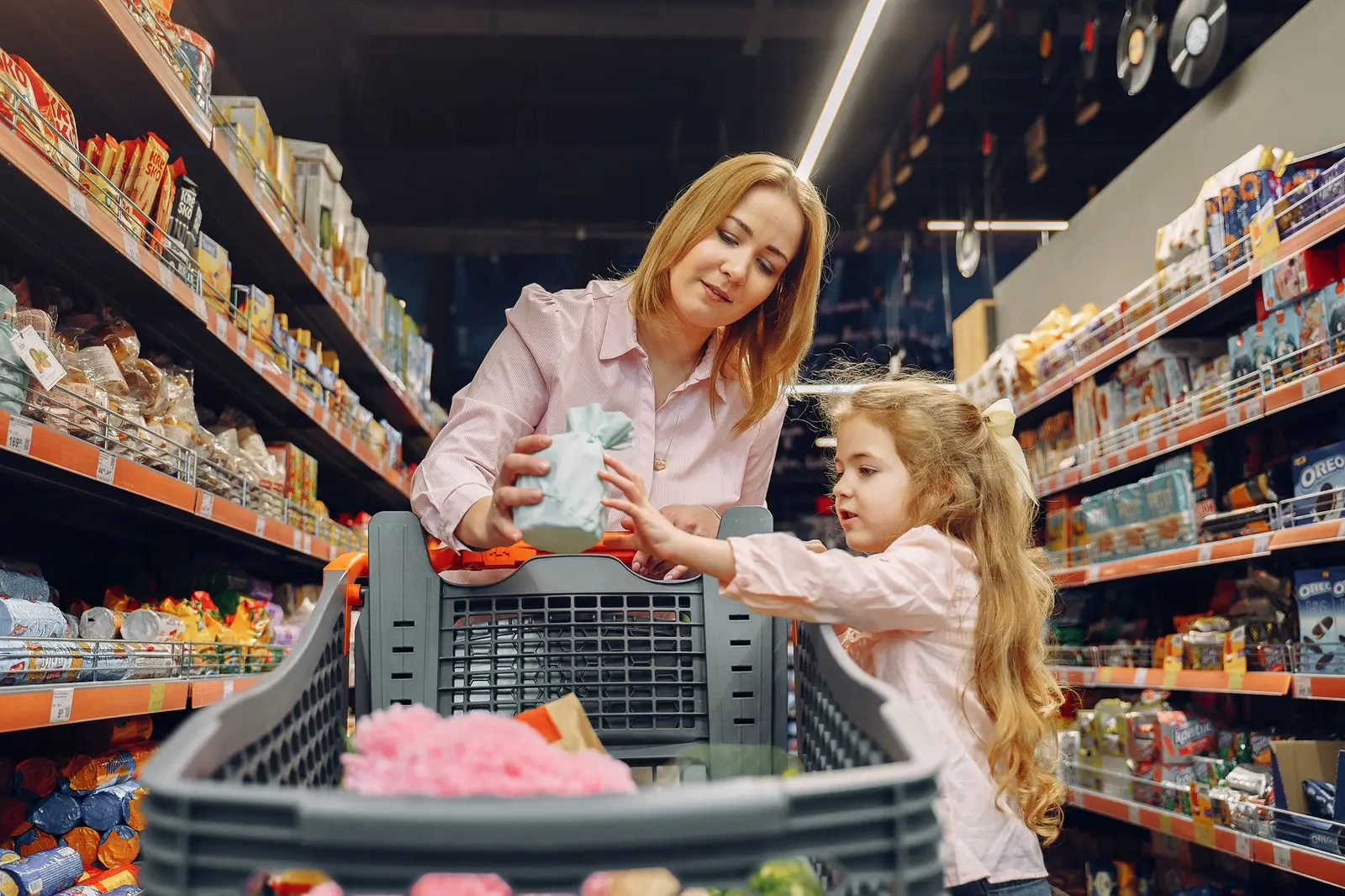 A mother and daughter choosing items from a supermarket shelf with a cart