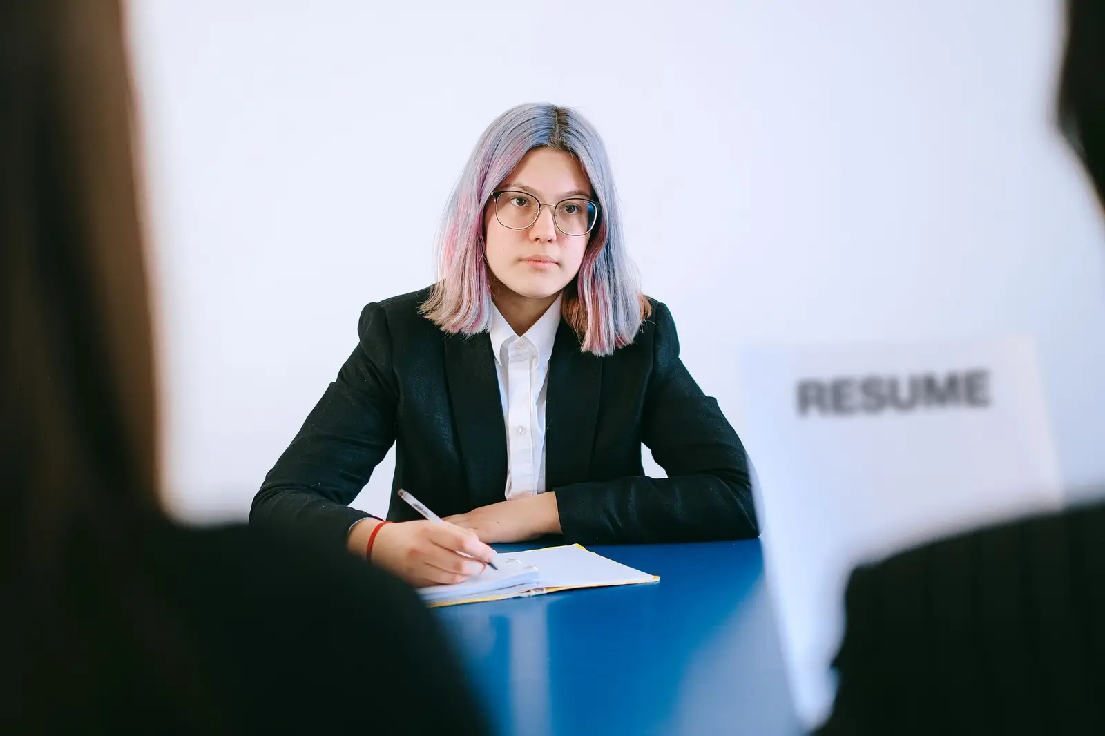 A young woman in a suit writing notes during a job interview