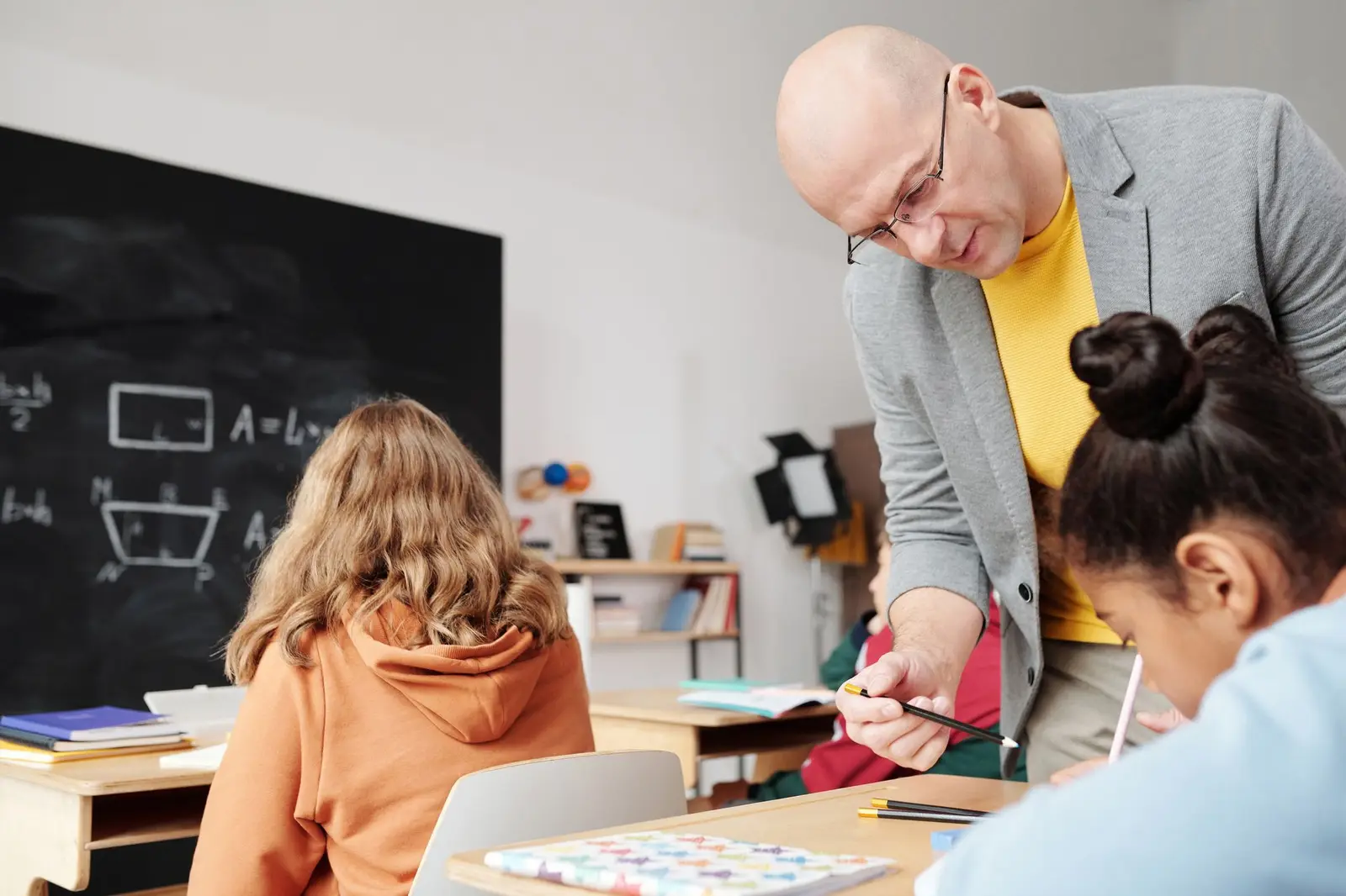 A teacher leaning over to help two students with their work at their desks