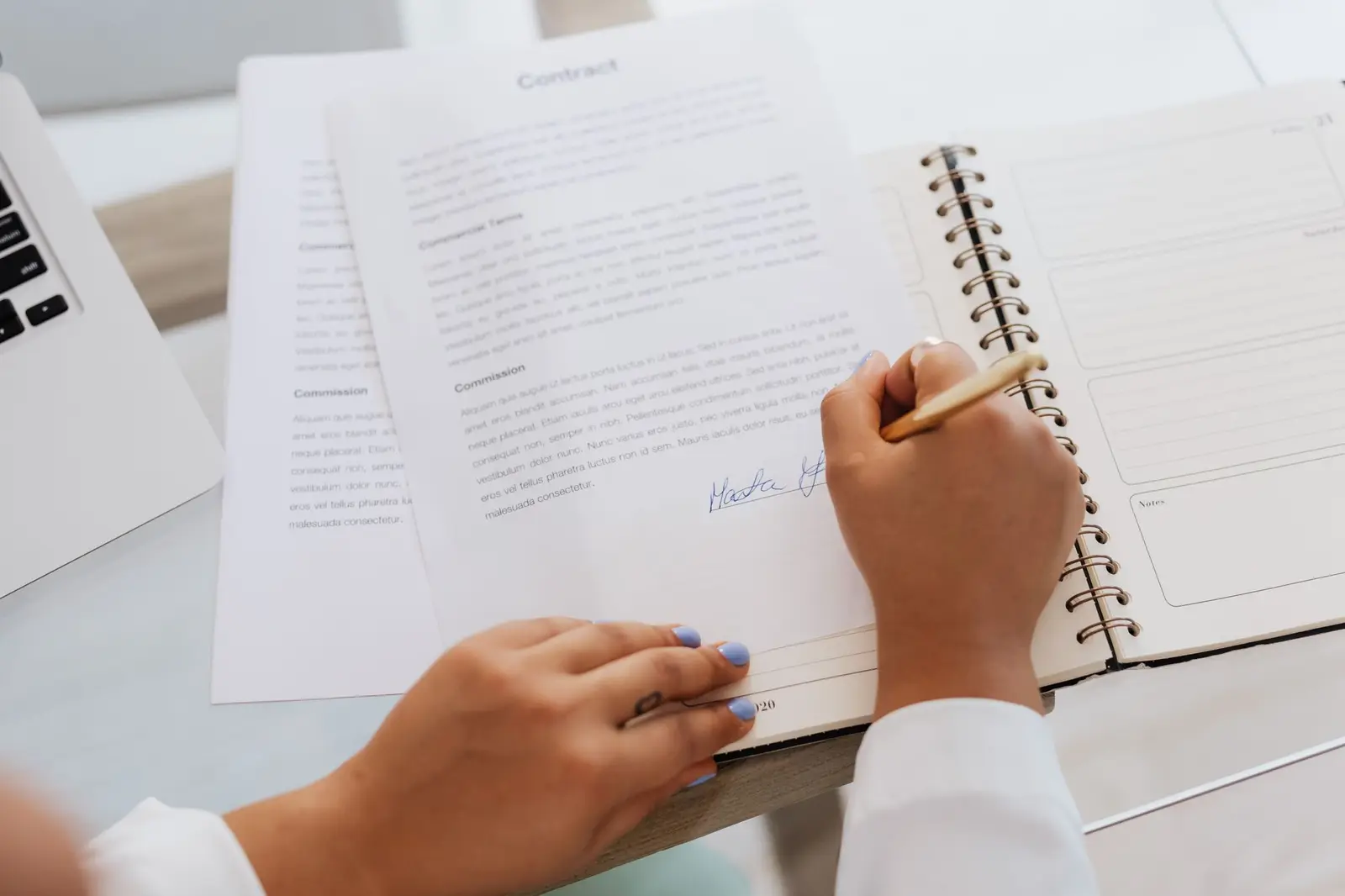 A person signing a document beside a notebook