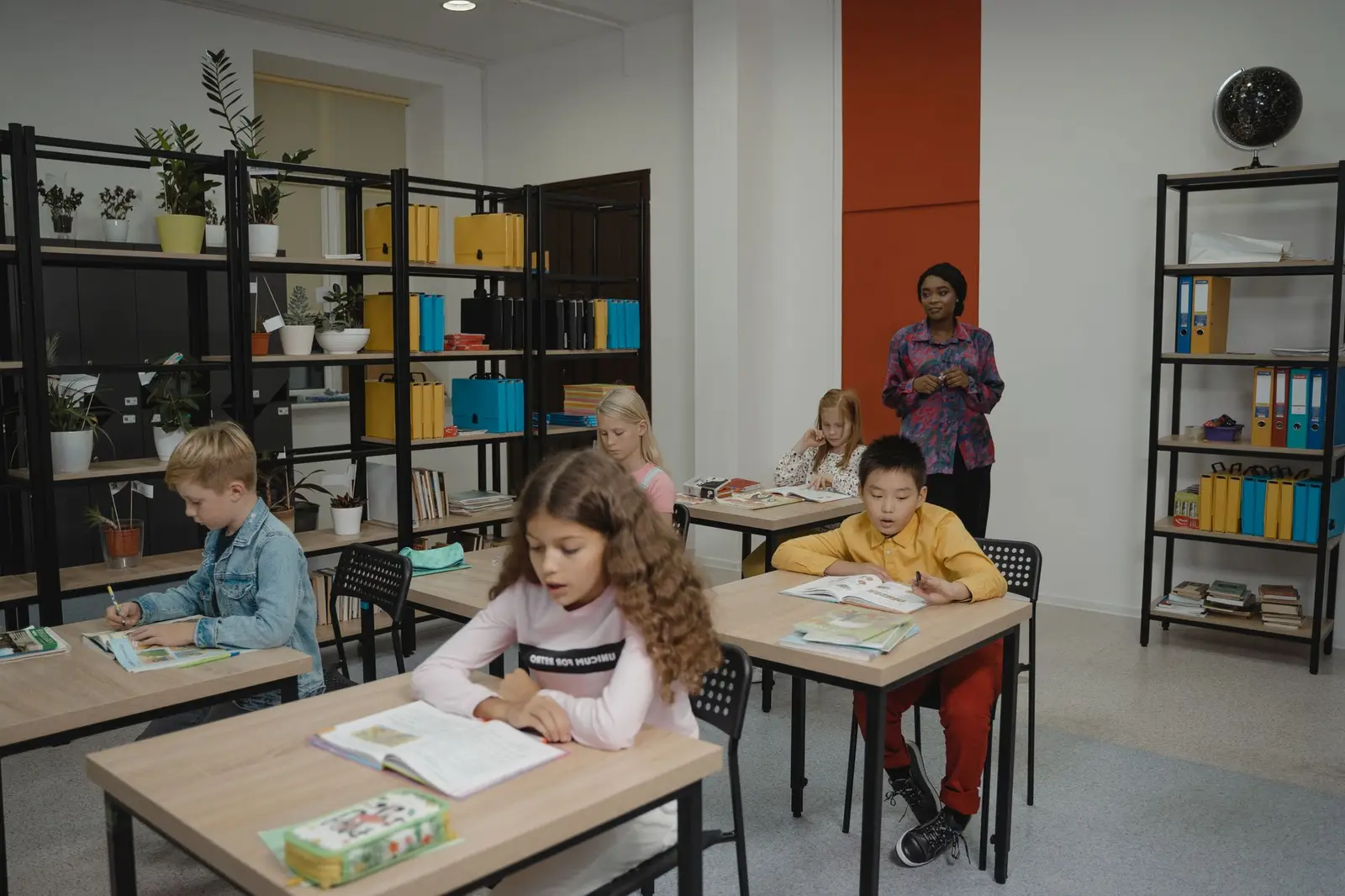 Primary students working at desks while a teacher watches over the classroom