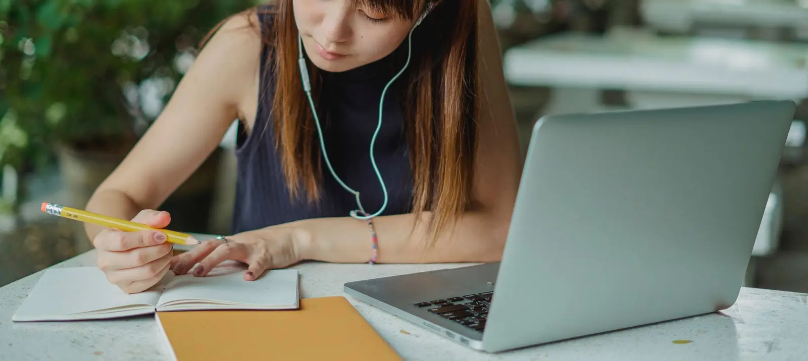 A young woman taking notes while studying with a laptop