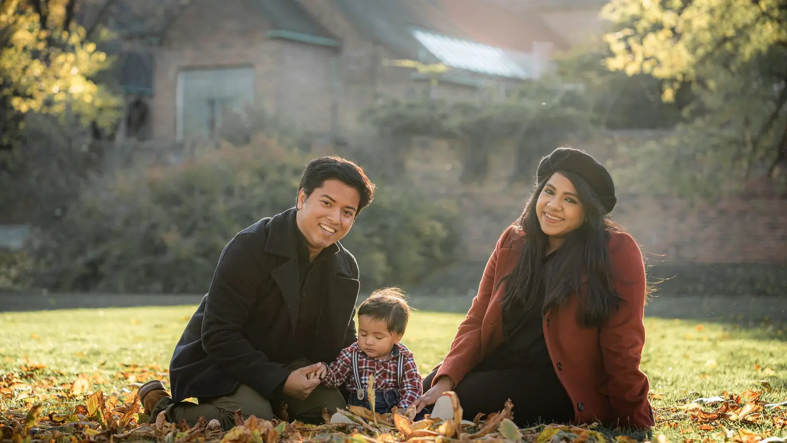 Two parents and a toddler sitting together in autumn leaves