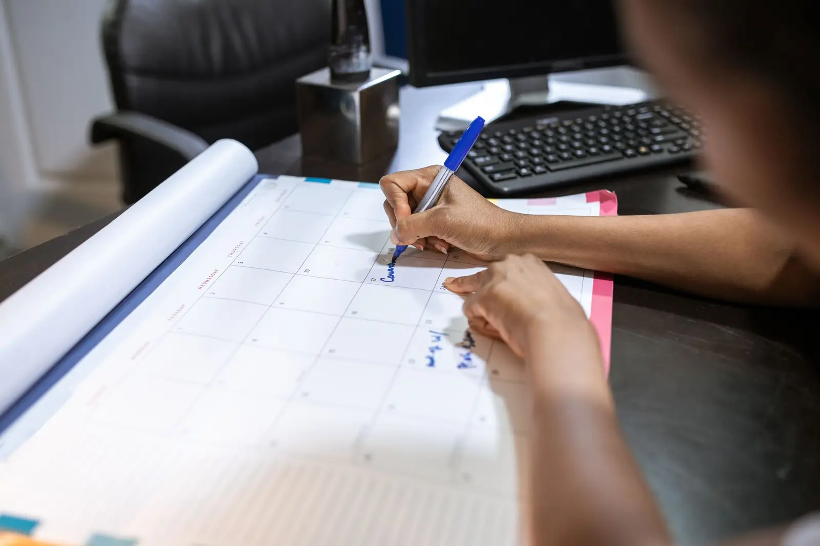 A person writing plans on a large desk calendar