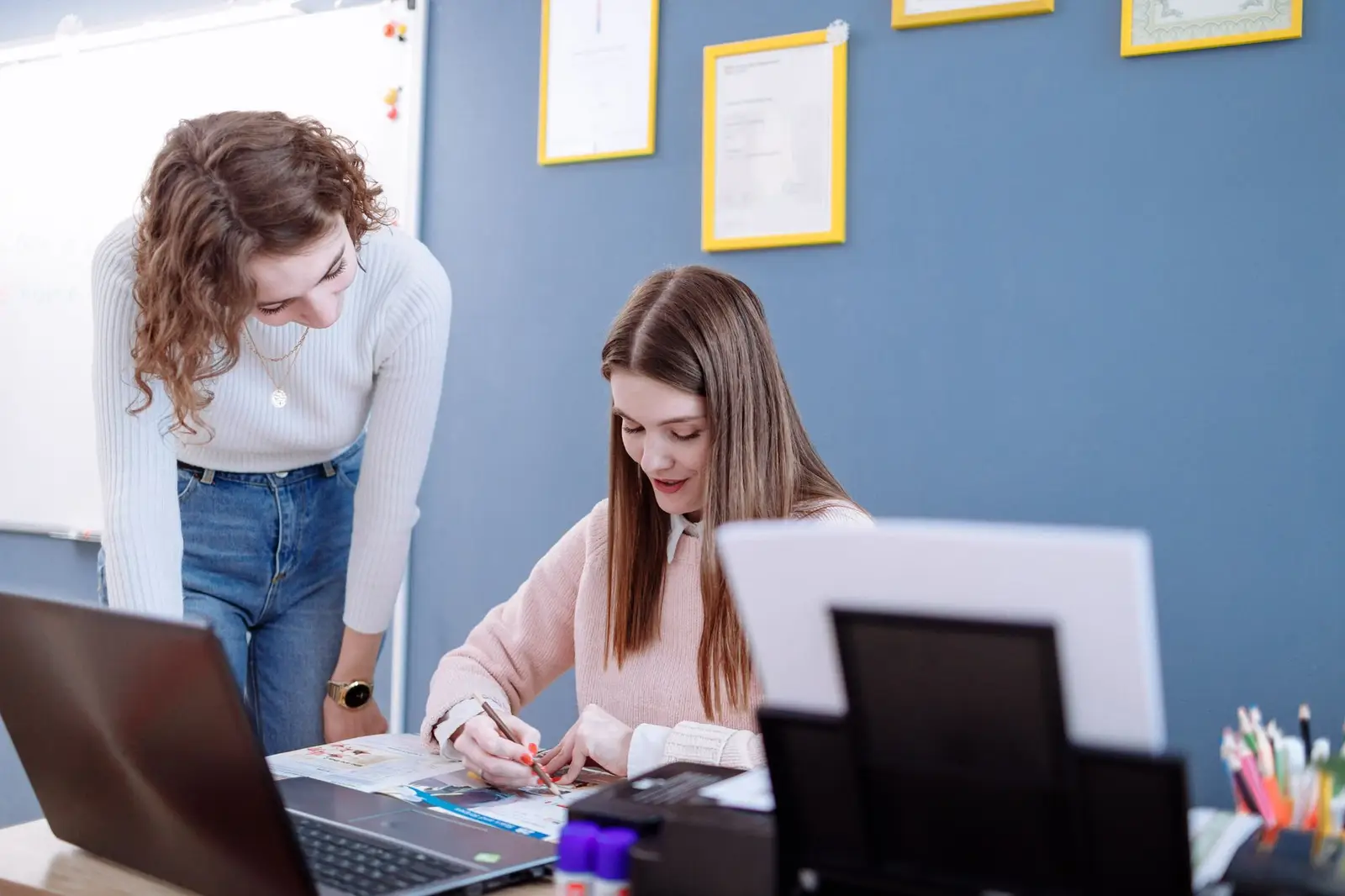 Two women working together on materials at a desk in a bright room
