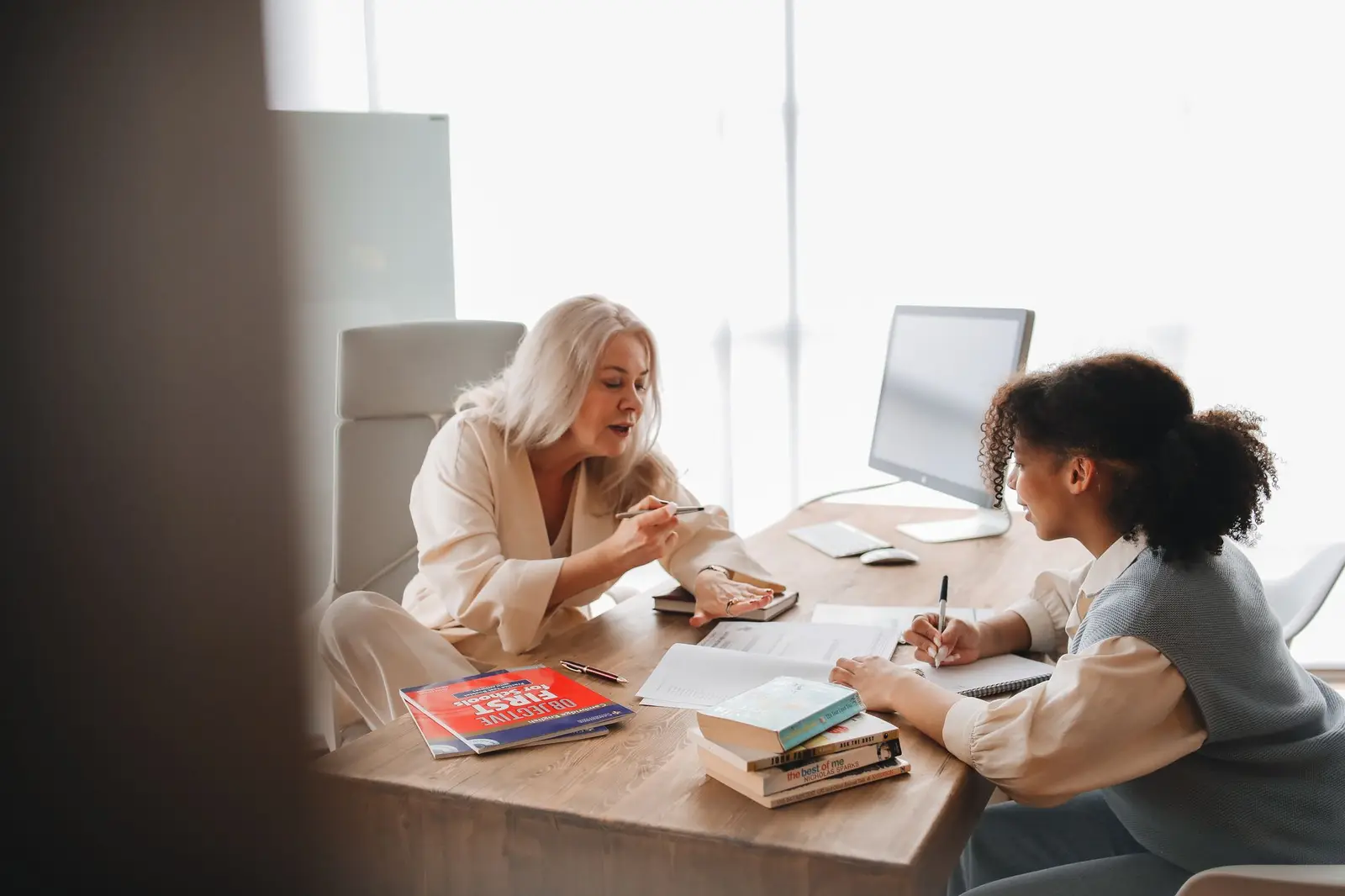 An educator talking with a student across a desk covered with books