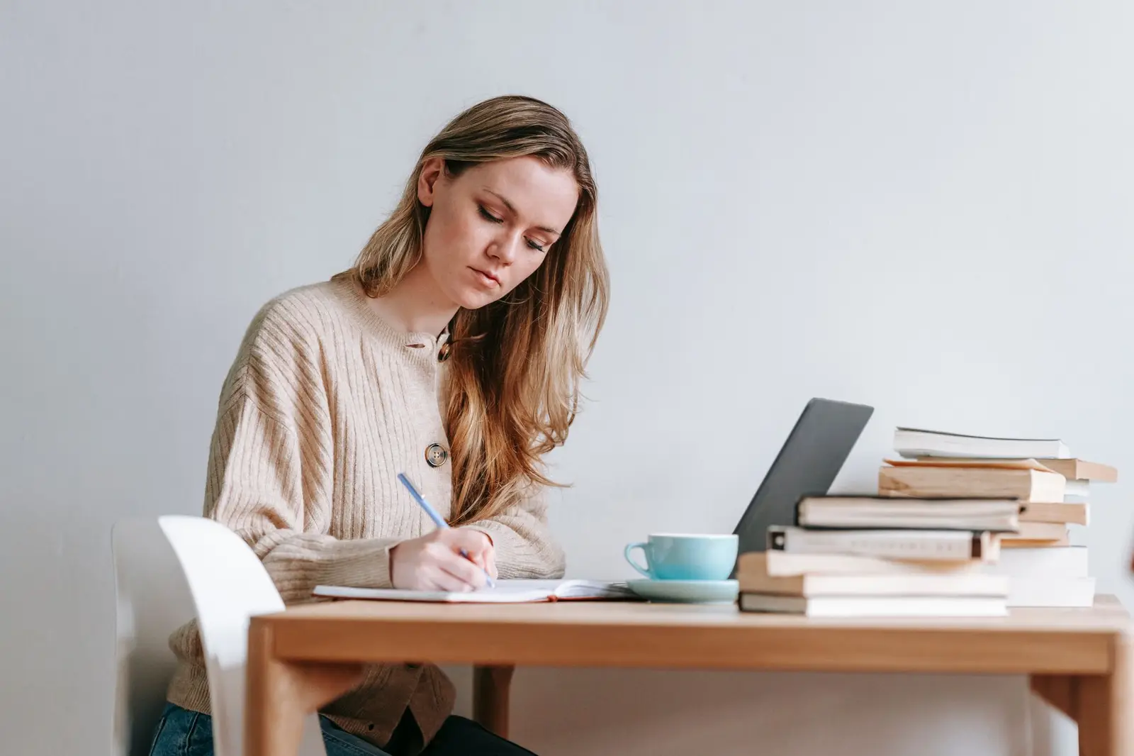 A woman writing notes in a planner at a desk with a laptop and stacked books