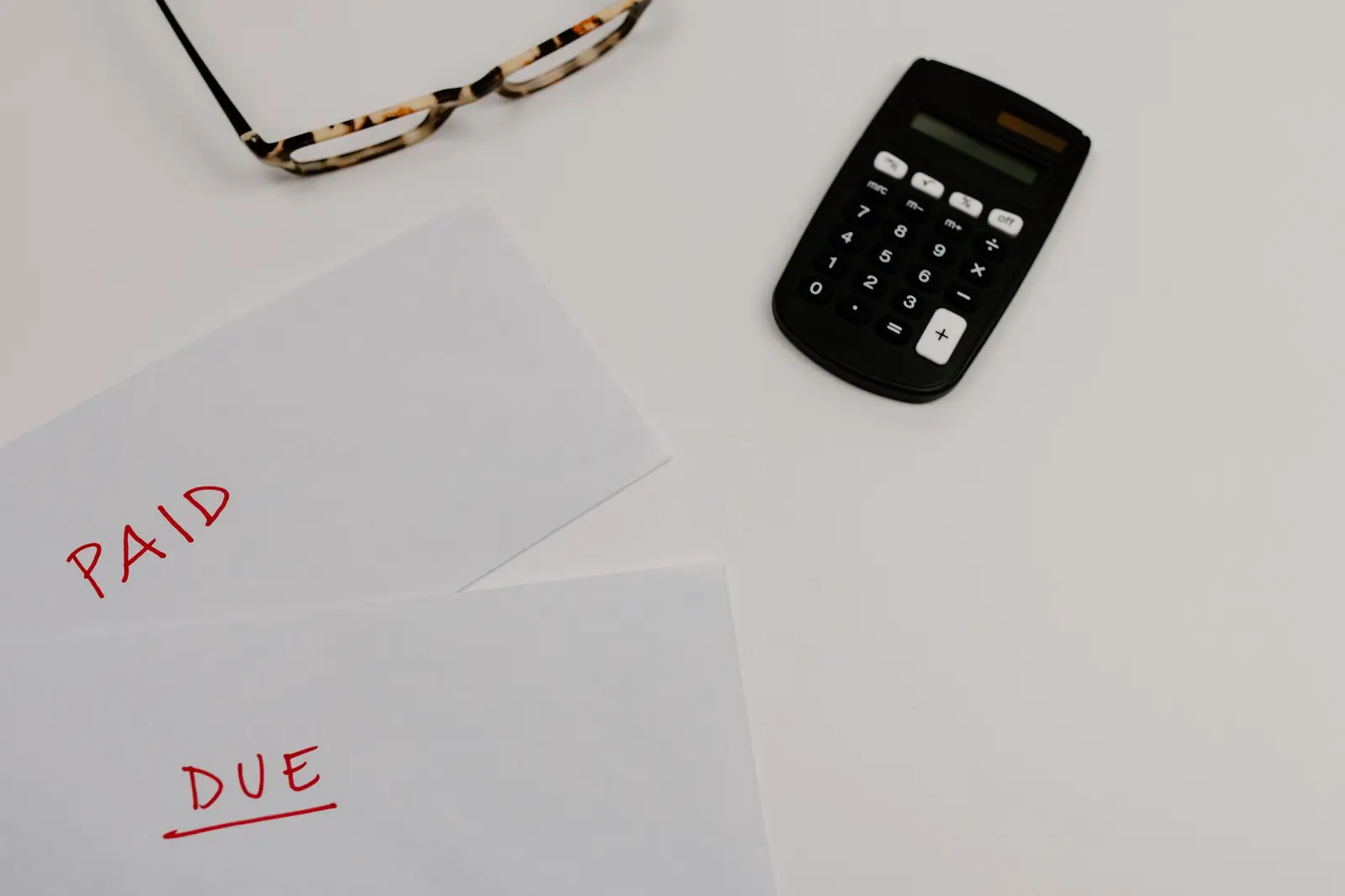 A calculator, glasses and bills marked paid and due on a desk