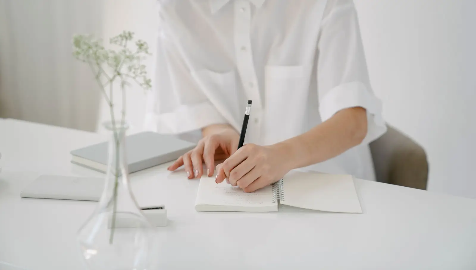 A person writing notes in a notebook at a white desk