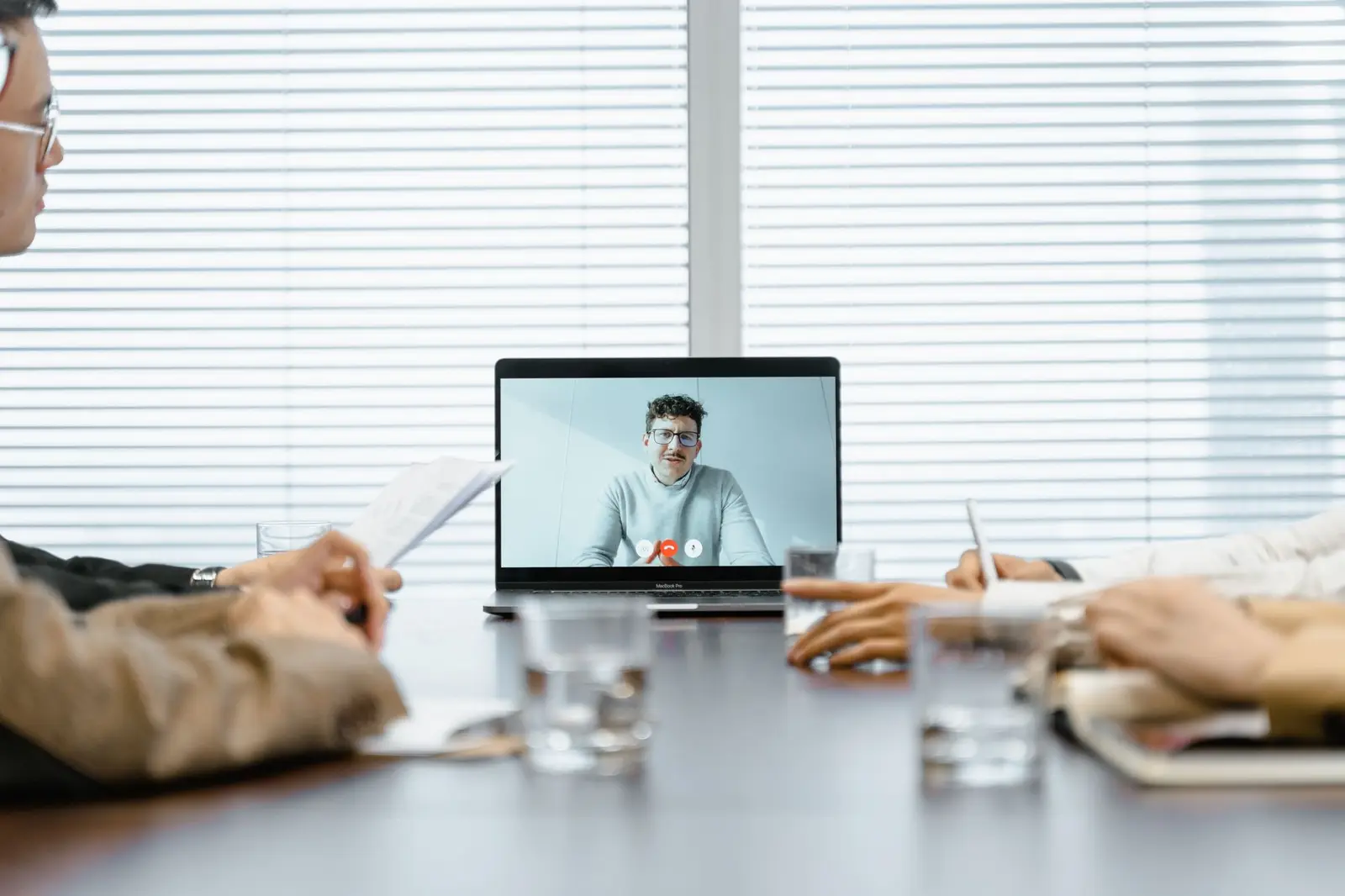 A team meeting around a table with a colleague on a video call