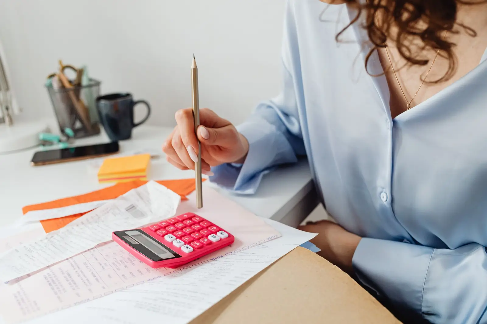 A woman working through paperwork with a pink calculator at a desk