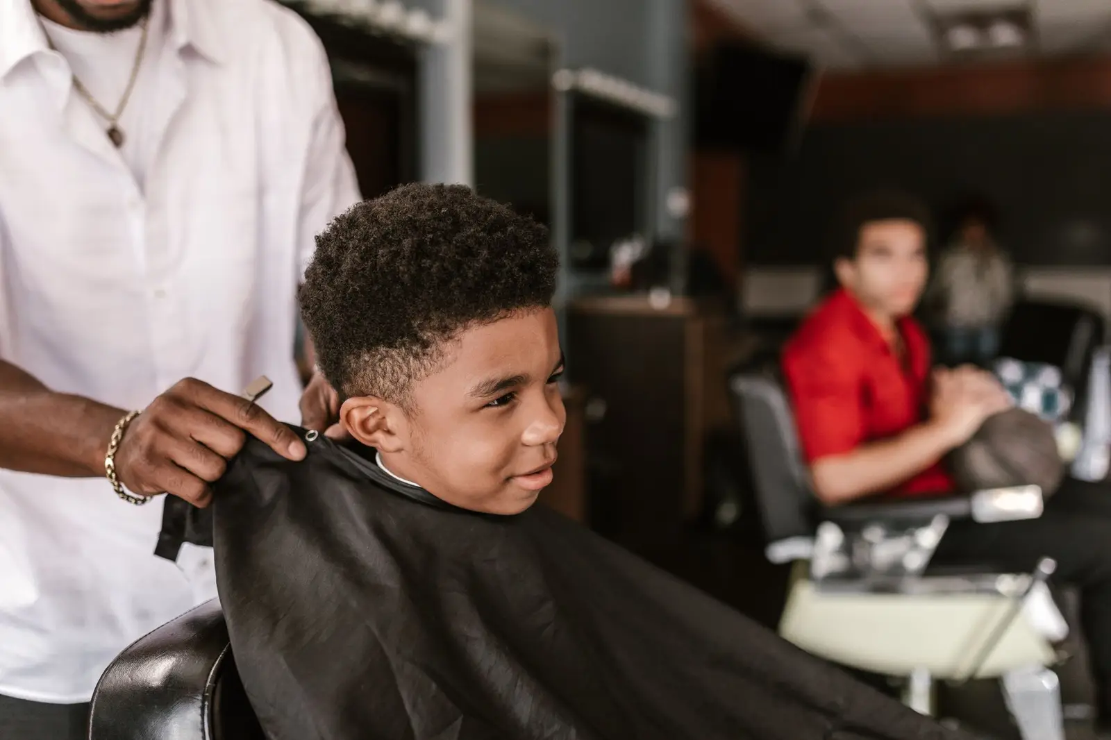 A barber putting a cape on a smiling boy in a barbershop