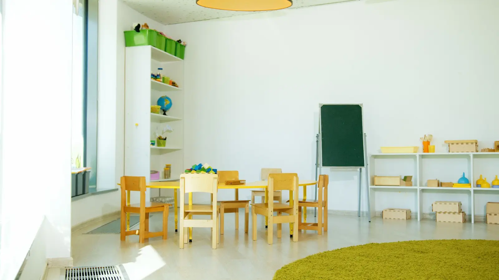 An empty, bright classroom with small chairs, tables and a green rug