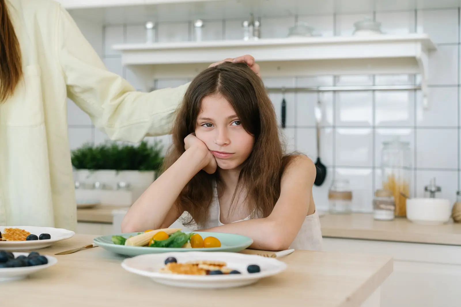 A girl resting her chin on her hand in front of a plate of breakfast