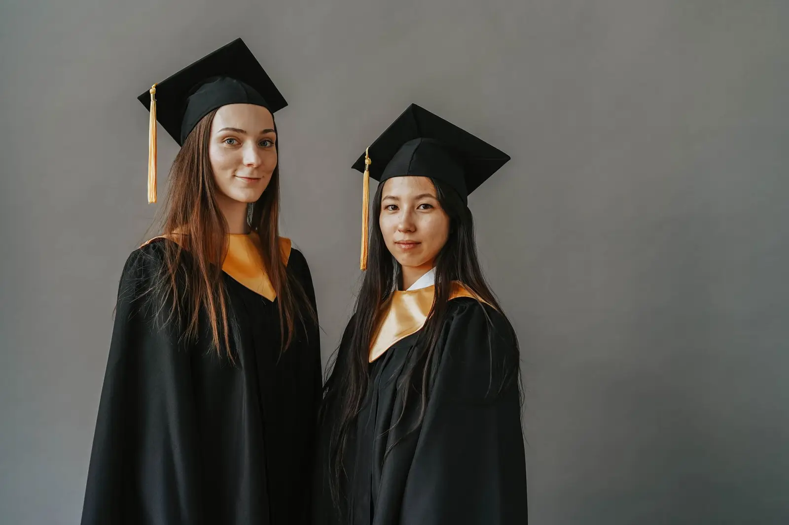 Two graduates in caps and gowns smiling together