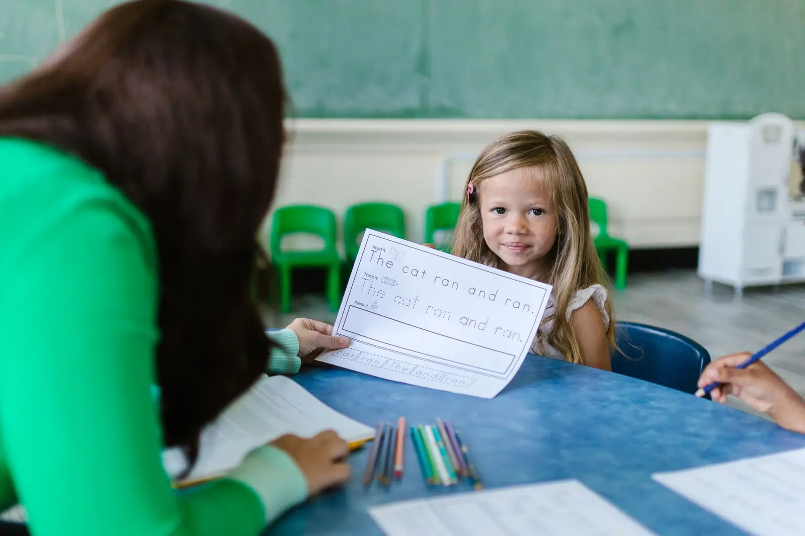 A teacher working with a young girl at a classroom table