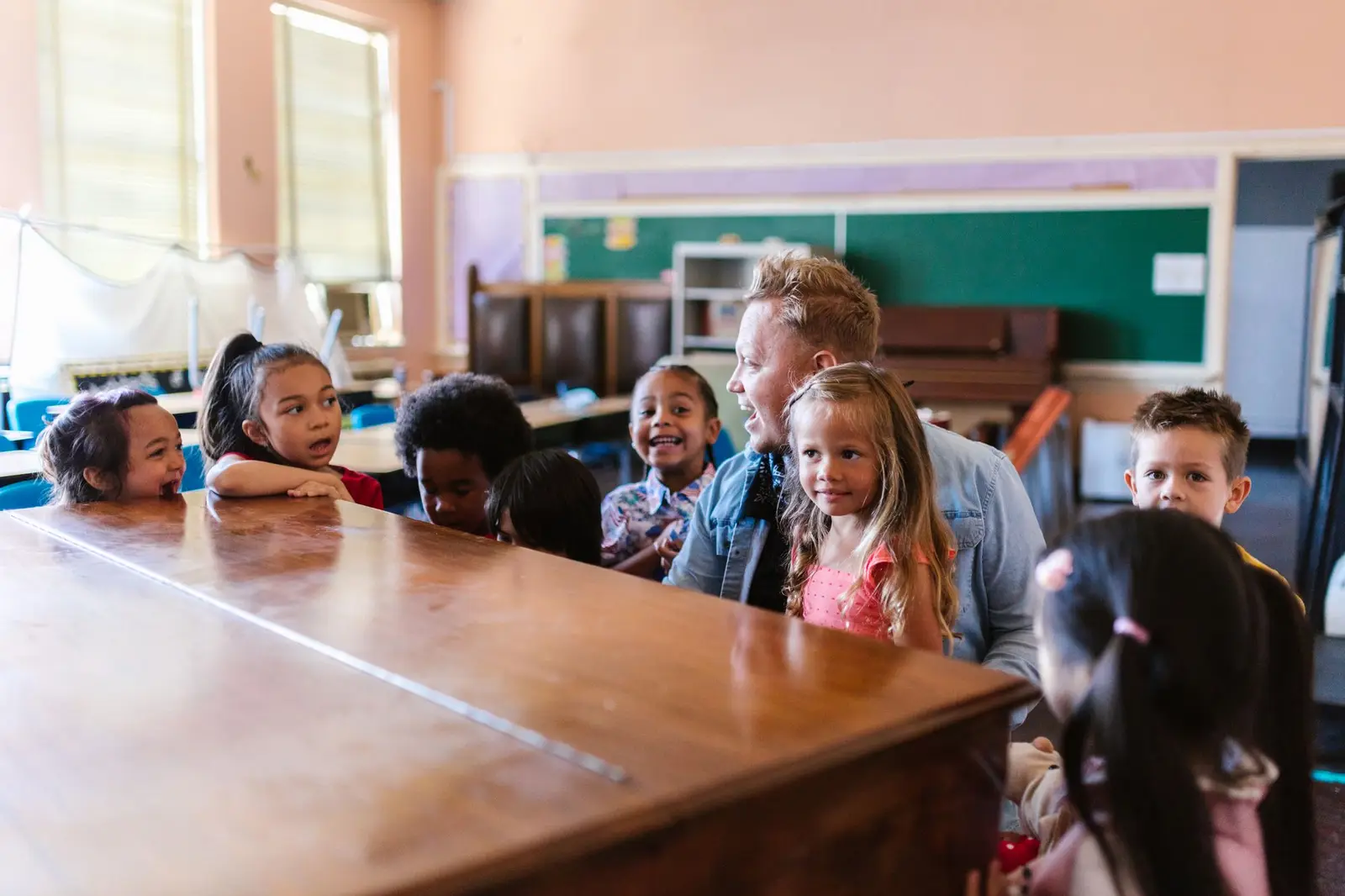 A teacher and a group of smiling children gathered around a table in a classroom