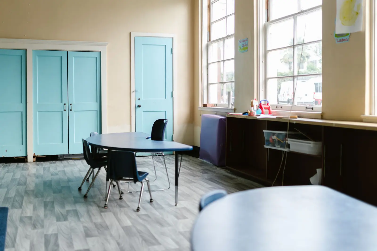 An empty, bright classroom with blue doors, a round table and chairs