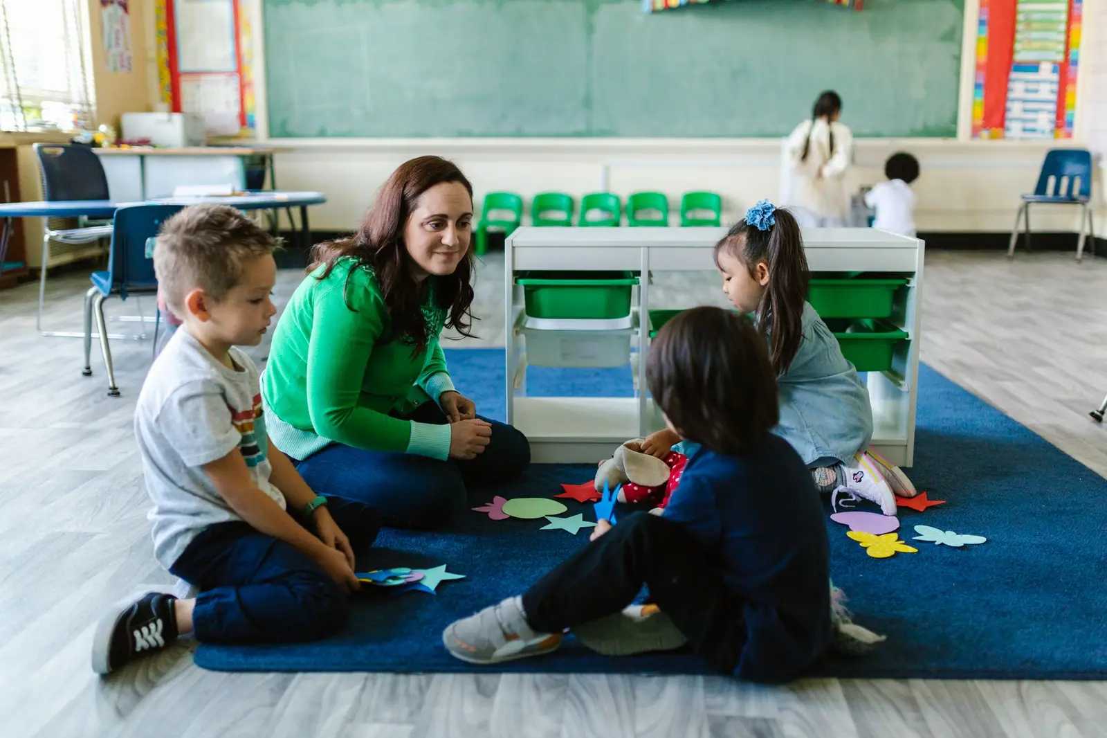 A teacher sitting on a rug doing an activity with young children