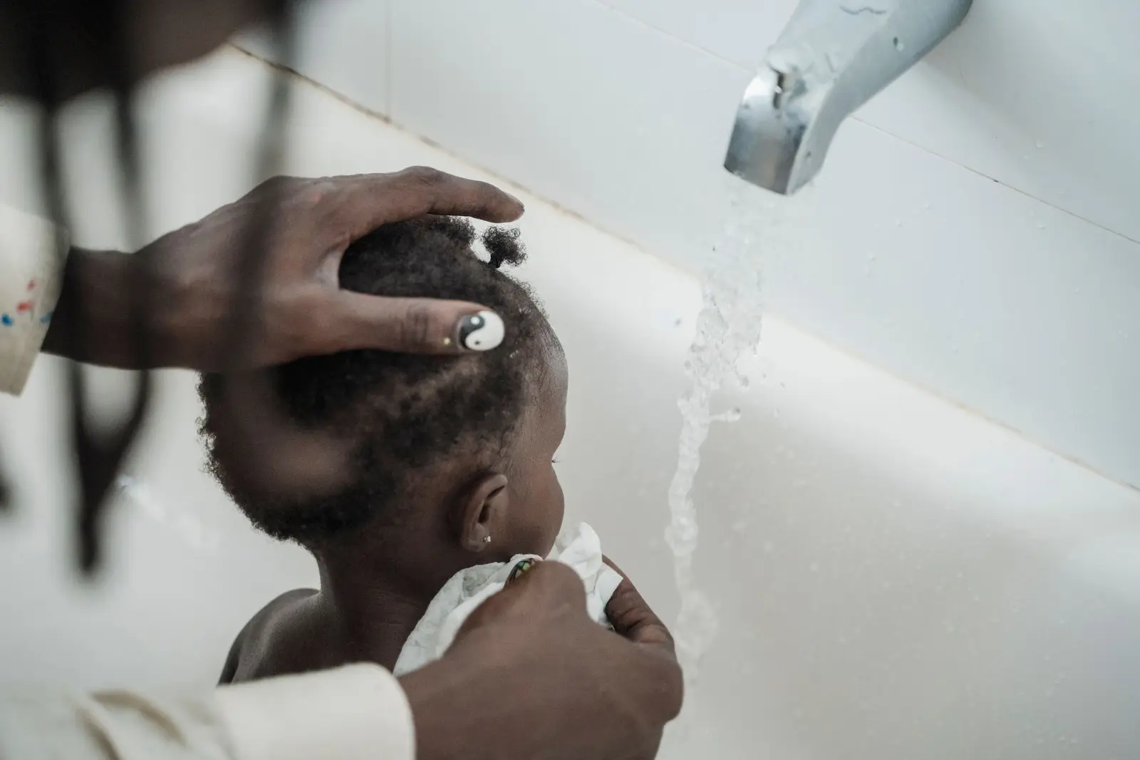 A parent washing a toddler's hair under a running bath tap