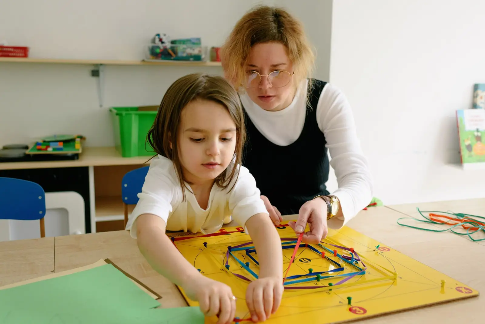 A teacher helping a young girl with a hands-on learning activity at a table