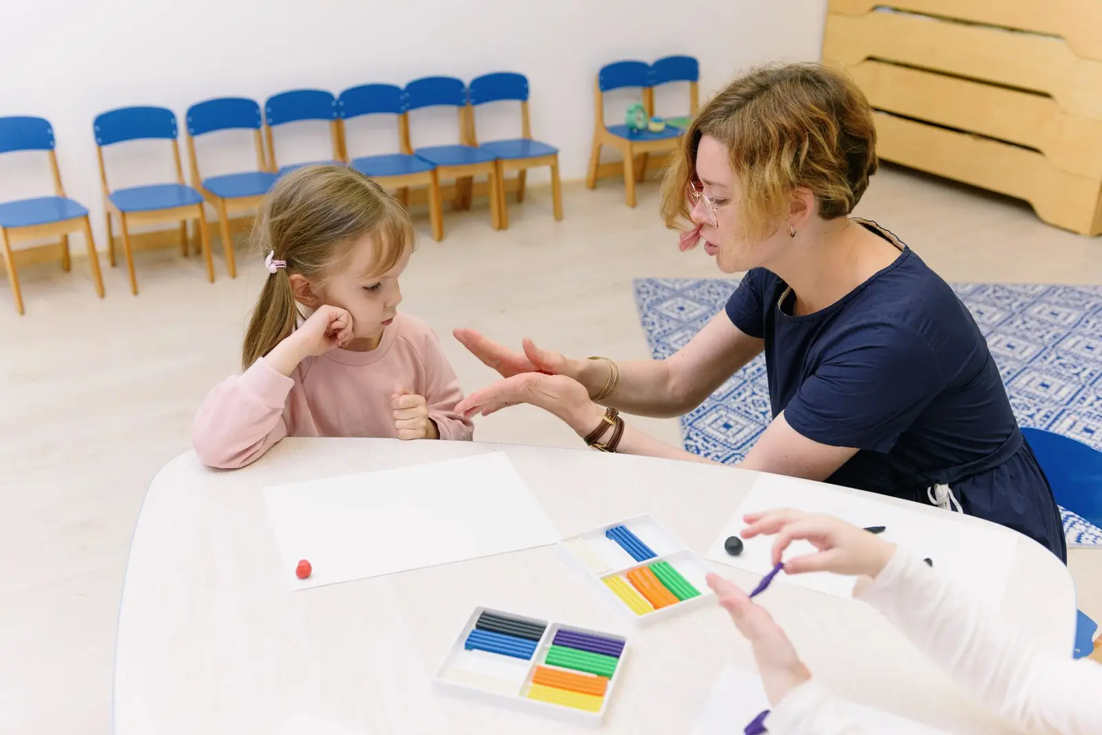 A teacher helping a young girl with a clay activity at a classroom table
