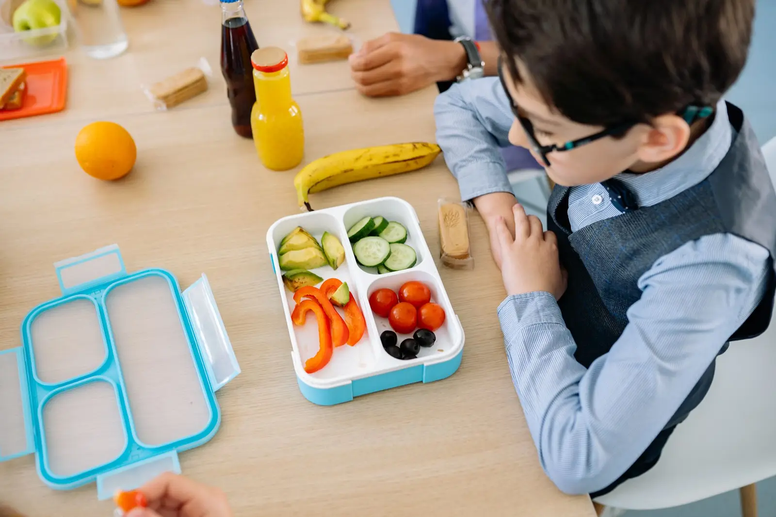 A boy eating a healthy lunch from a colourful lunch box at a school table