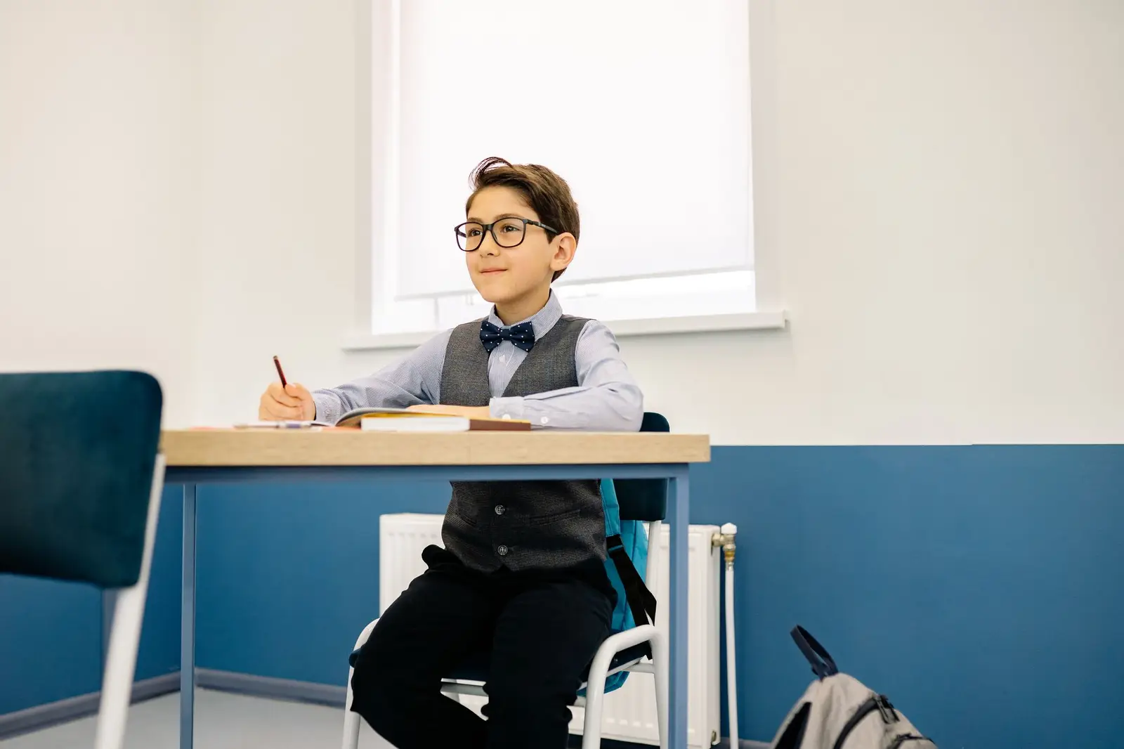 A boy in glasses and a bow tie sitting at a school desk ready to learn