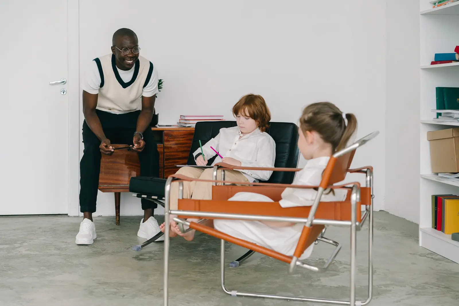 An educator talking with two children sitting in chairs in a bright room