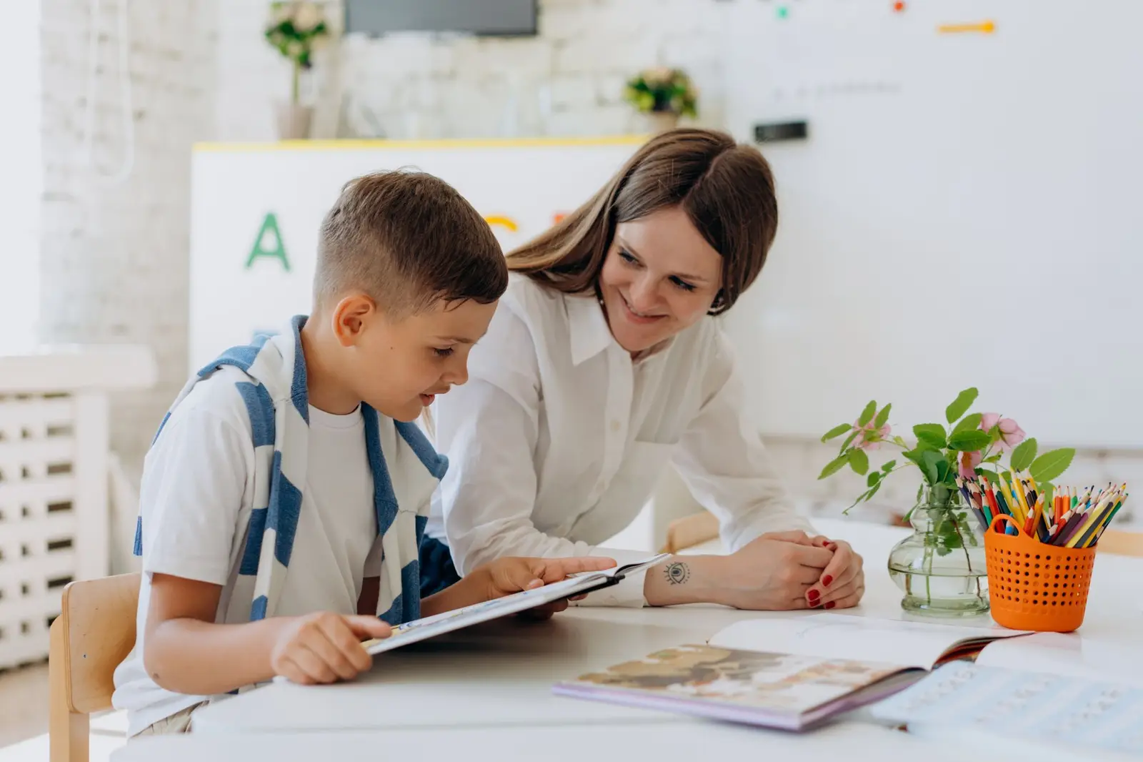 A teacher helping a boy use a tablet at a classroom table