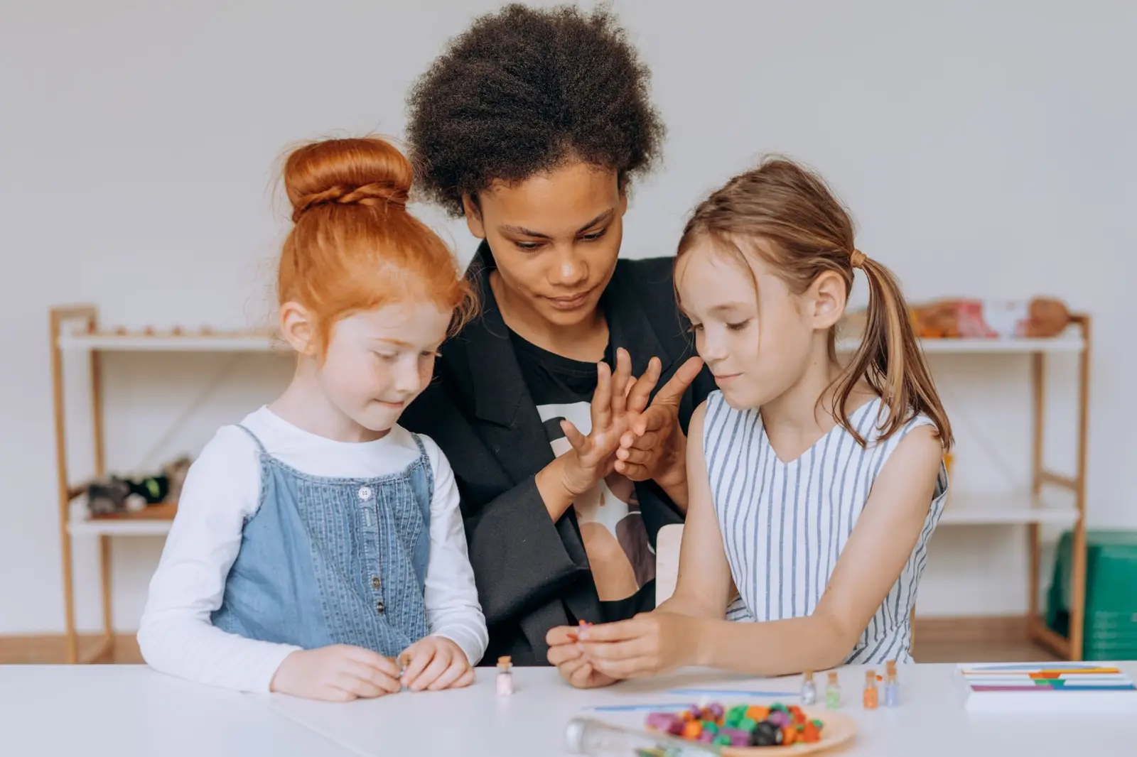 A teacher guiding two girls through a hands-on activity at a table