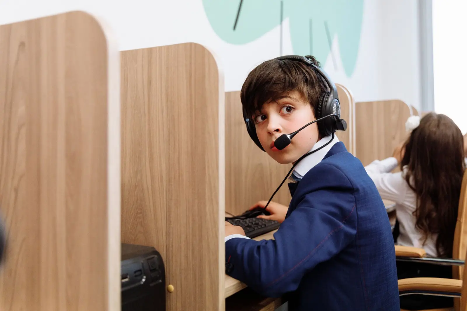 A boy wearing a headset looking back from a study booth in a classroom