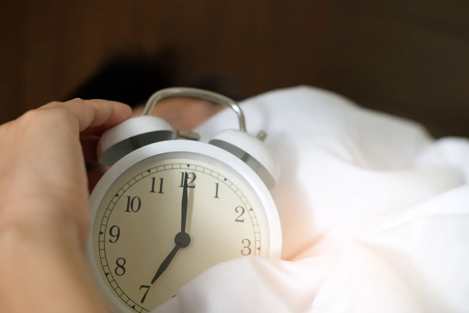 A hand reaching for an alarm clock on a bed