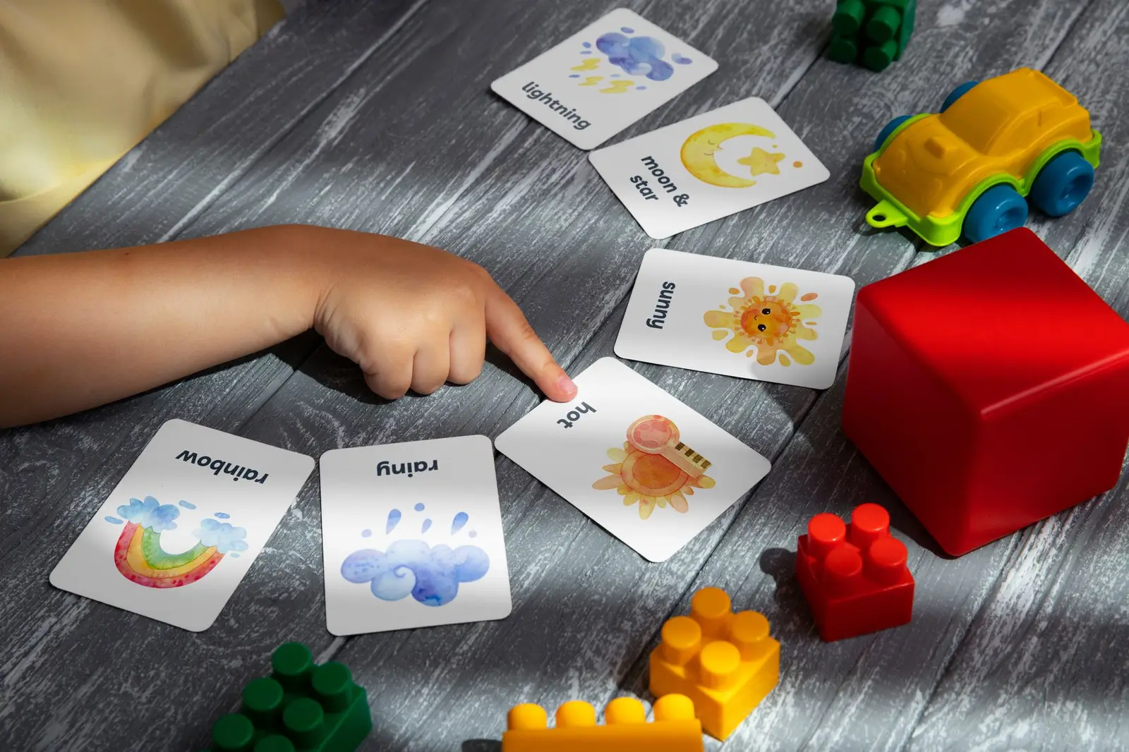 A child pointing at colorful picture cards on a table with toy blocks