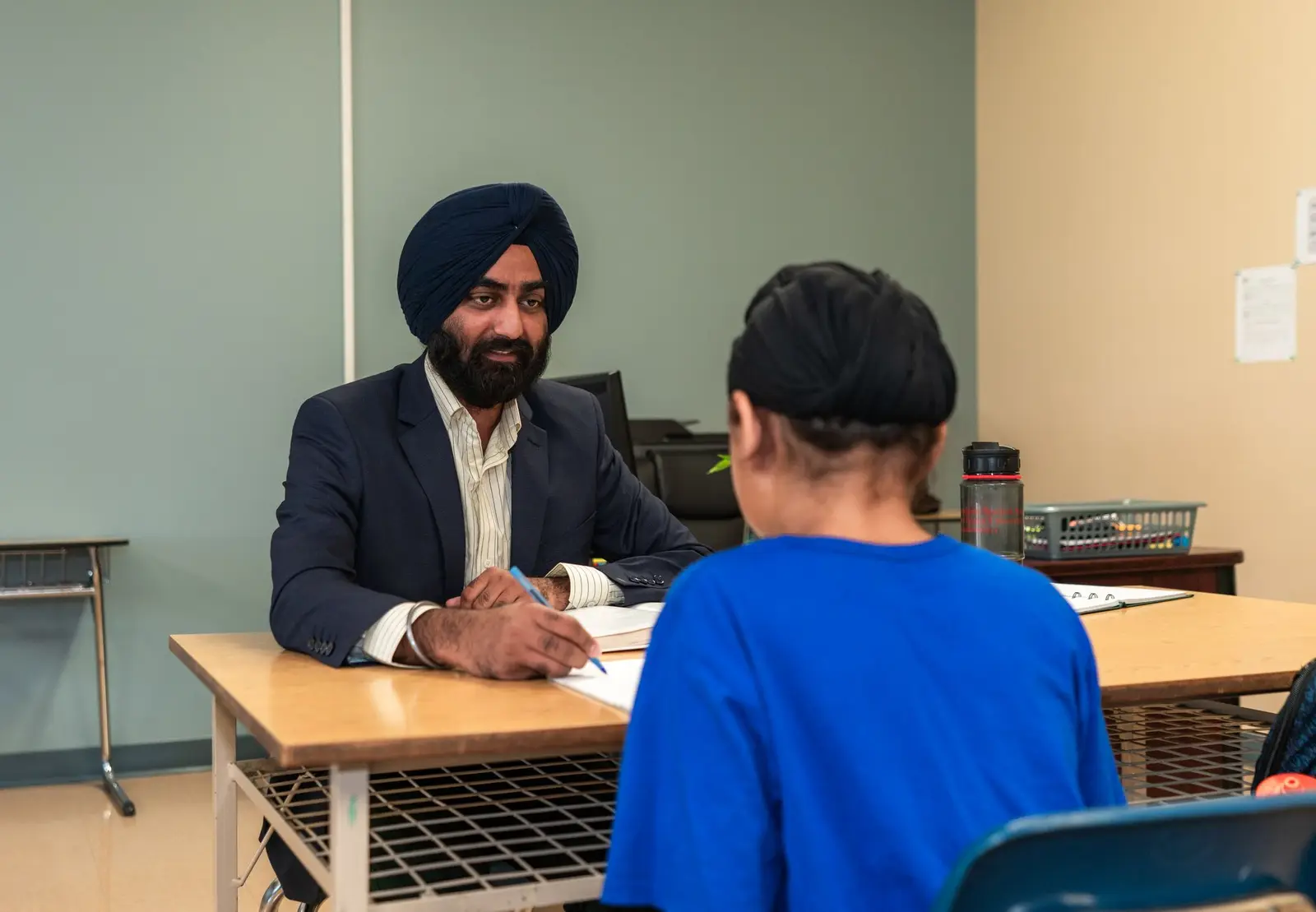 A teacher smiling as he talks one-to-one with a pupil at a classroom desk
