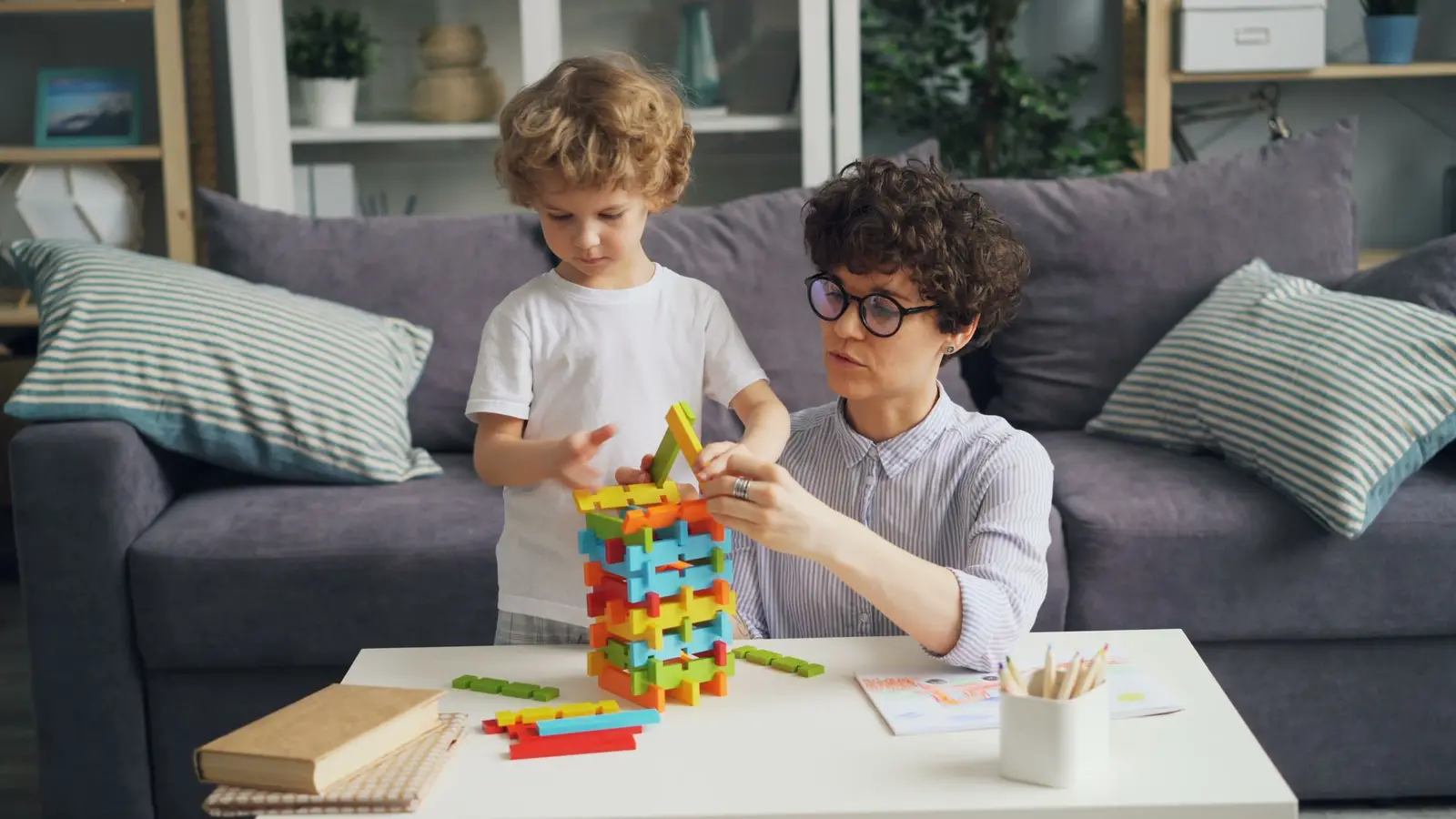 A mother and her young son building a colorful block tower together at a coffee table