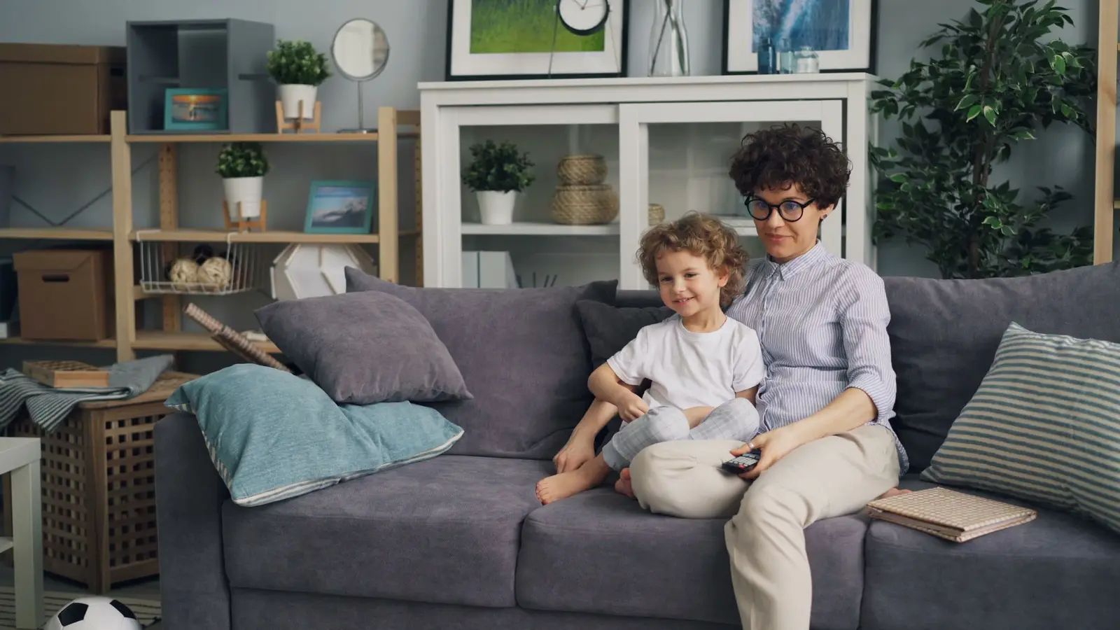 A parent and young child sitting together on a grey sofa at home