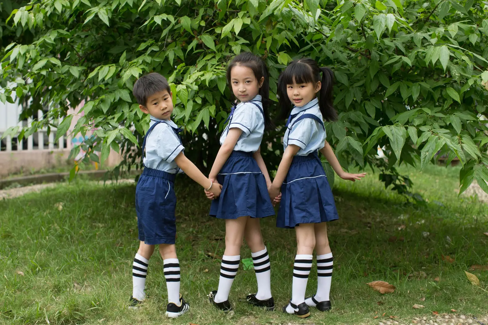 Three young children in school uniforms holding hands outdoors