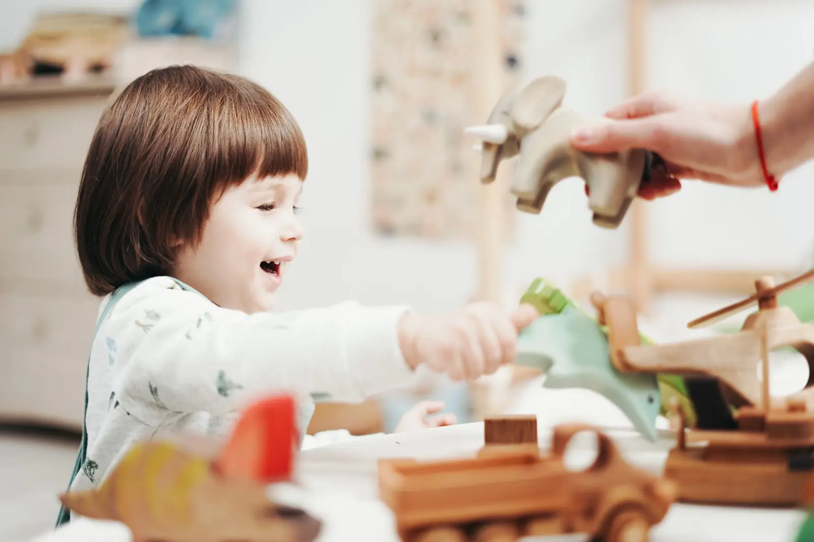 A smiling child reaching for wooden toys on a table