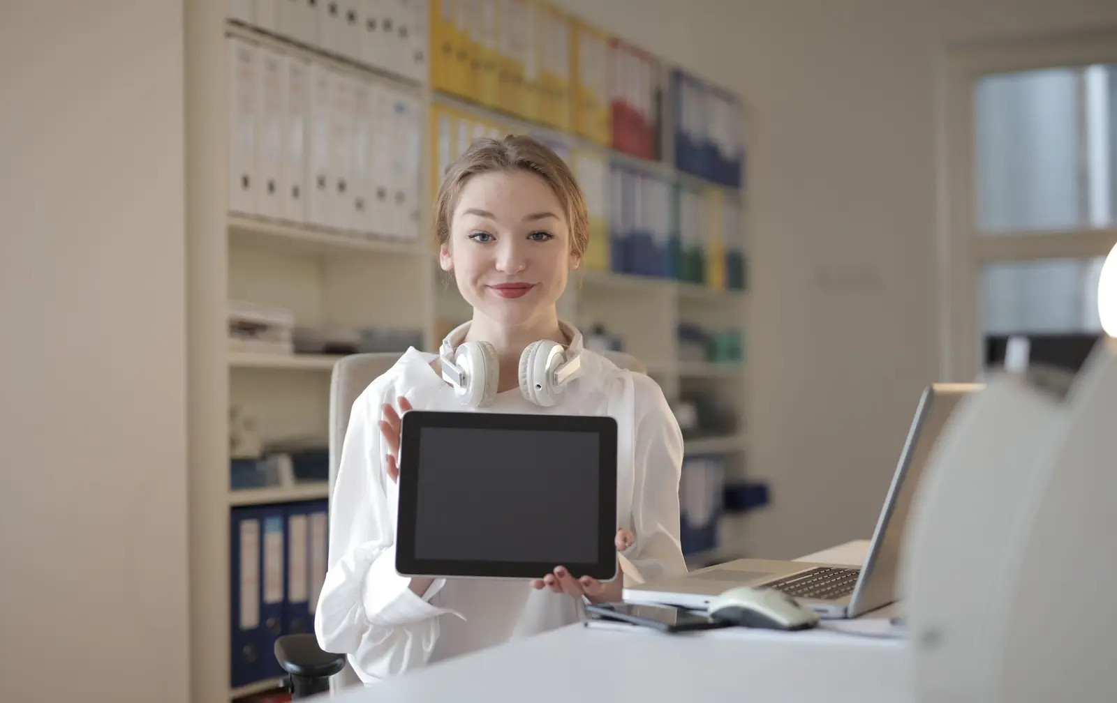 A smiling woman holding a tablet in a bright office