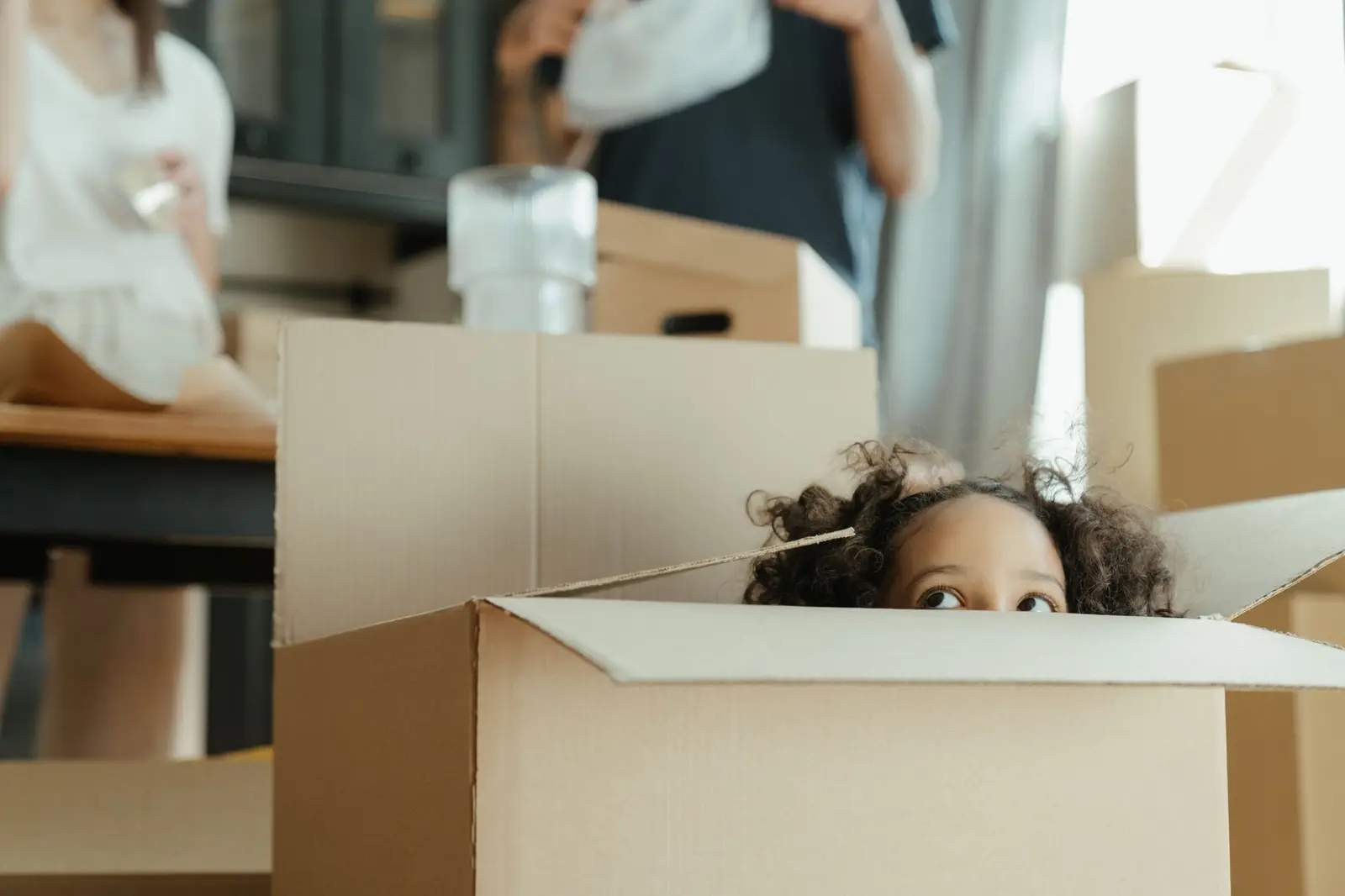 A child peeking out of a cardboard box among moving boxes