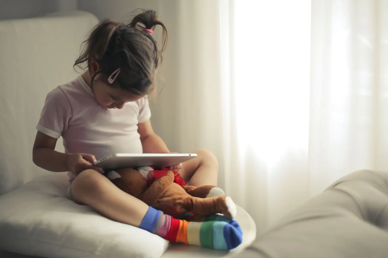 A young girl sitting on a sofa using a tablet