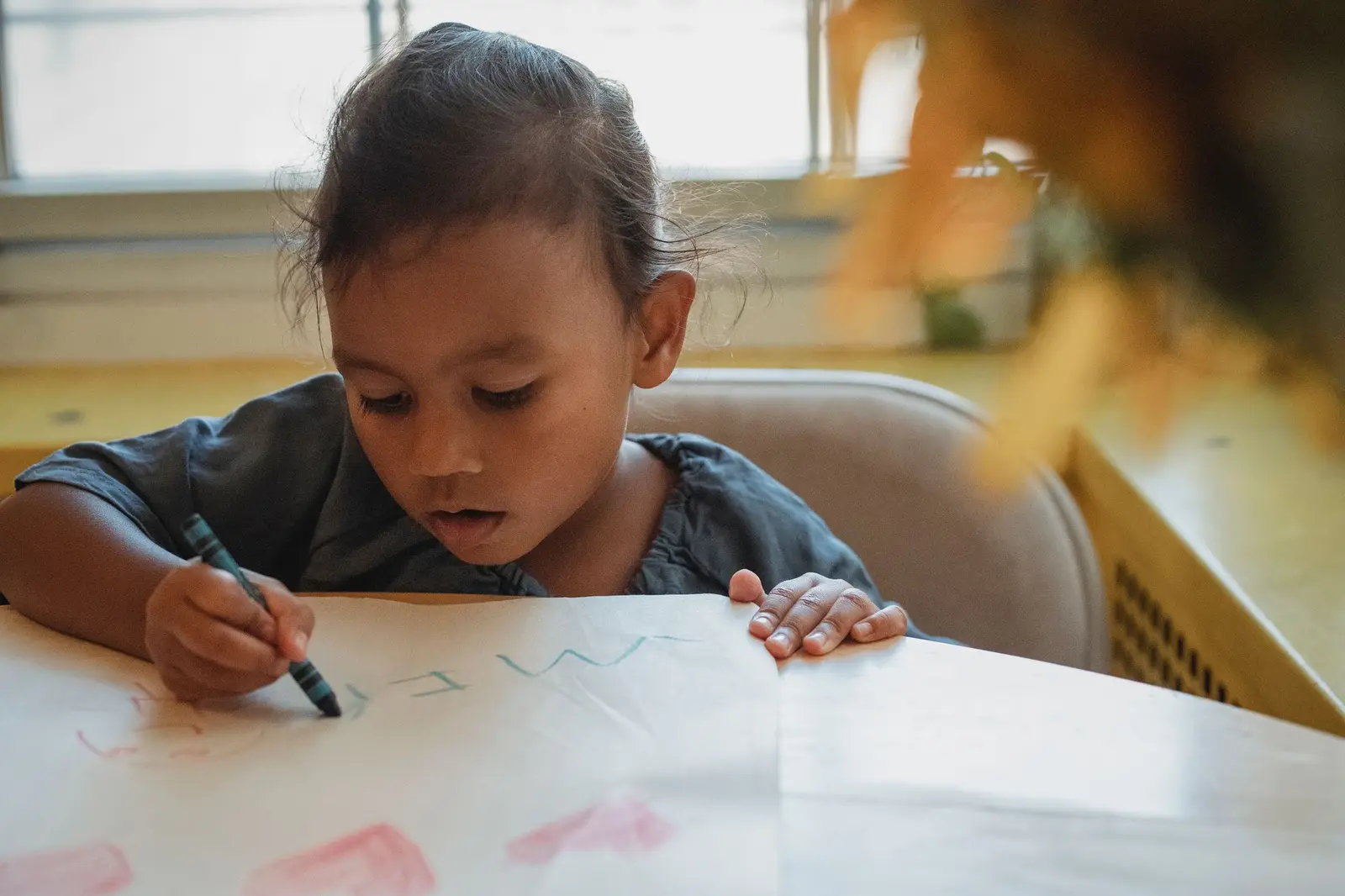 A young girl concentrating as she draws with a crayon at a table
