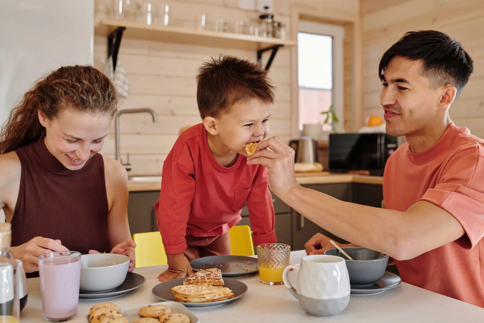 A family of three laughing over breakfast in the kitchen